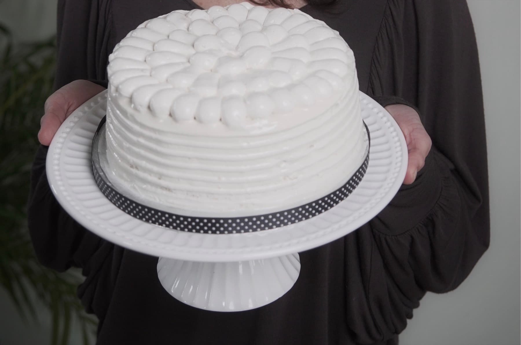 Leonor holding a white frosted cake on a cake stand